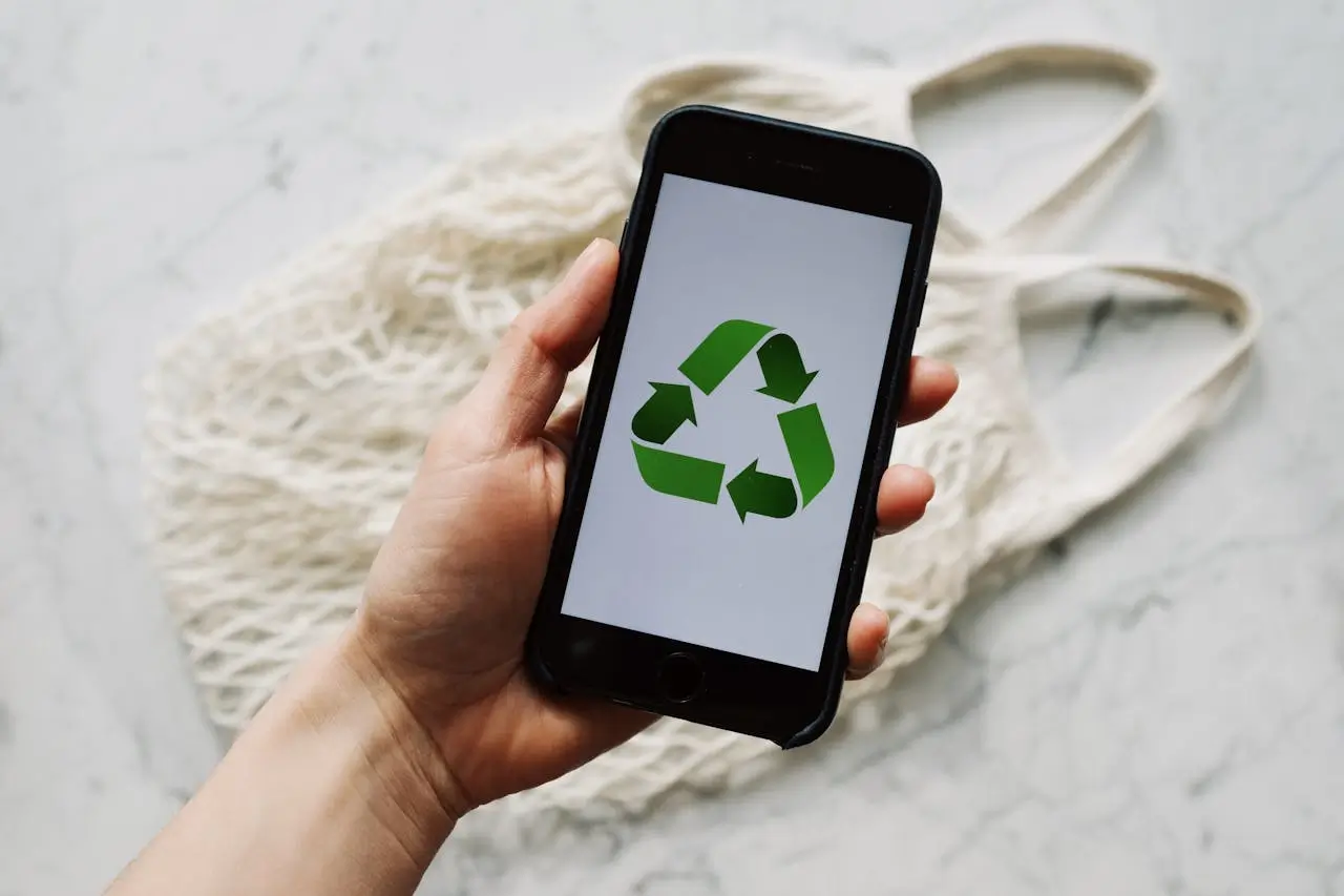 Person's hand holding mobile phone showing a green recycle logo